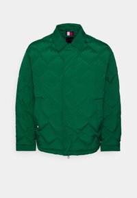 Giacca trapuntata verde con colletto, dotata di chiusura con zip e una finitura morbida e testurizzata. Design minimalista senza hardware visibile.