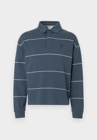 Μπλε μπλούζα πόλο με μακριά μανίκια και λευκές οριζόντιες ρίγες, γιακά με κουμπιά και μικρό κεντημένο λογότυπο στο αριστερό στήθος.