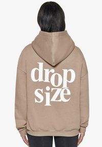 Beige Kapuzenpullover mit weißem Text "drop size" auf dem Rücken, ausgestattet mit einer geräumigen Kapuze und gerippten Bündchen, hergestellt aus einem weichen, strukturierten Stoff.