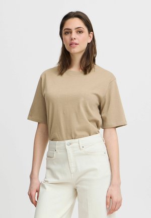 T-shirt in cotone beige con scollatura rotonda e maniche corte, abbinato a jeans in denim bianco a vita alta con tasche frontali e chiusura a bottone.