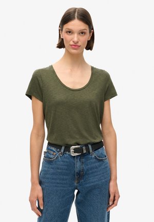 Maglietta verde oliva con scollatura rotonda e maniche corte, abbinata a jeans blu a vita alta e una cintura nera con fibbia d'argento.