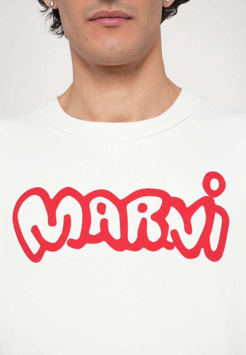 Vit t-shirt med kort ärm som har en stor, djärv röd "MARNI"-logga i ett lekfullt, rundat typsnitt. Slät bomullstextur.