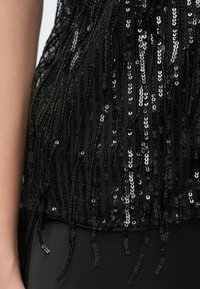 Mustast litritega top, millel on tutidetailid, tekstureeritud võrkkiht allosas ja peegeldavad litrid, luues läikiva efekti.