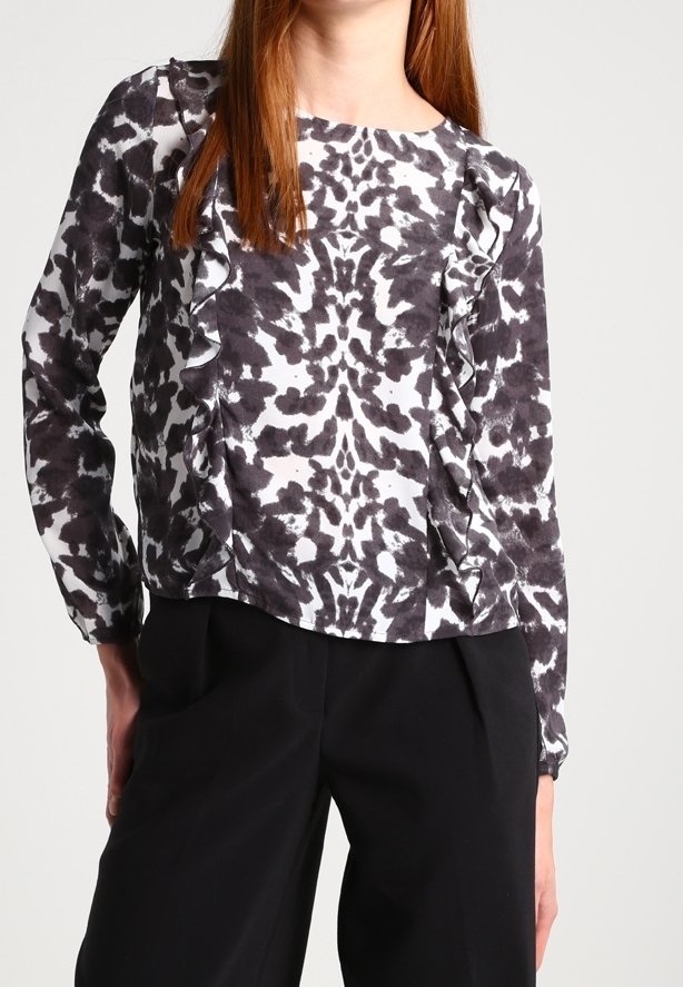 Blusa a maniche lunghe con motivo in bianco e nero, con cuciture laterali arricciate, abbinata a pantaloni neri.