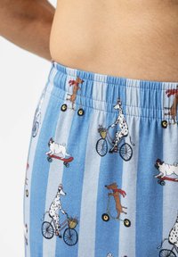 Baumwollshorts mit blau gestreiftem Muster und verspielten Hundeillustrationen, die Fahrrad und Scooter fahren. Elastischer Bund, weiche Textur.