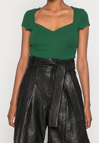 Groen geribd T-shirt met korte mouwen en een vierkante halslijn, gecombineerd met hooggewaisted zwarte leren broeken met een gestrikt taille detail.