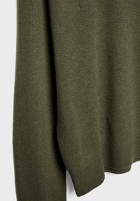 Gros plan sur un tissu tricoté vert olive montrant la texture et le poignet d'un vêtement à manches longues.