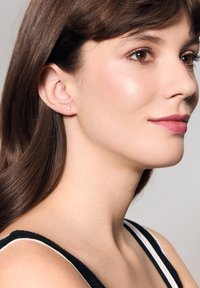 Kolczyki wkrętki mają mały, okrągły kamień przypominający diament osadzony w srebrnym tle, noszone przez modelkę z brązowymi włosami do ramion.