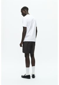 Black shorts, white t-shirt, white socks, and black shoes. The outfit features a relaxed fit, simple design, and minimalistic color palette.