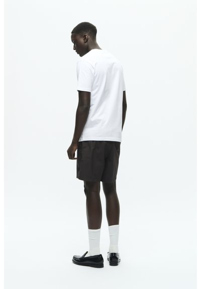 Pantaloni scurți negri, tricou alb, șosete albe și pantofi negri. Ținuta are o croială confortabilă, un design simplu și o paletă de culori minimalistă.