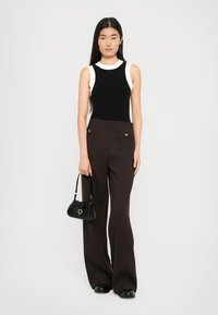Zwart-wit mouwloze top gecombineerd met high-waisted bruine flare broeken met gouden knopen en zijzakken. Zwarte handtas inbegrepen.