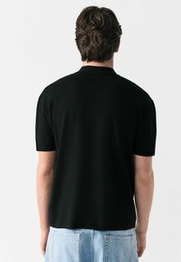 Sort kortærmet polo-shirt med en tekstureret overflade og en flad krave, kombineret med lyseblå denimshorts med to baglommer.
