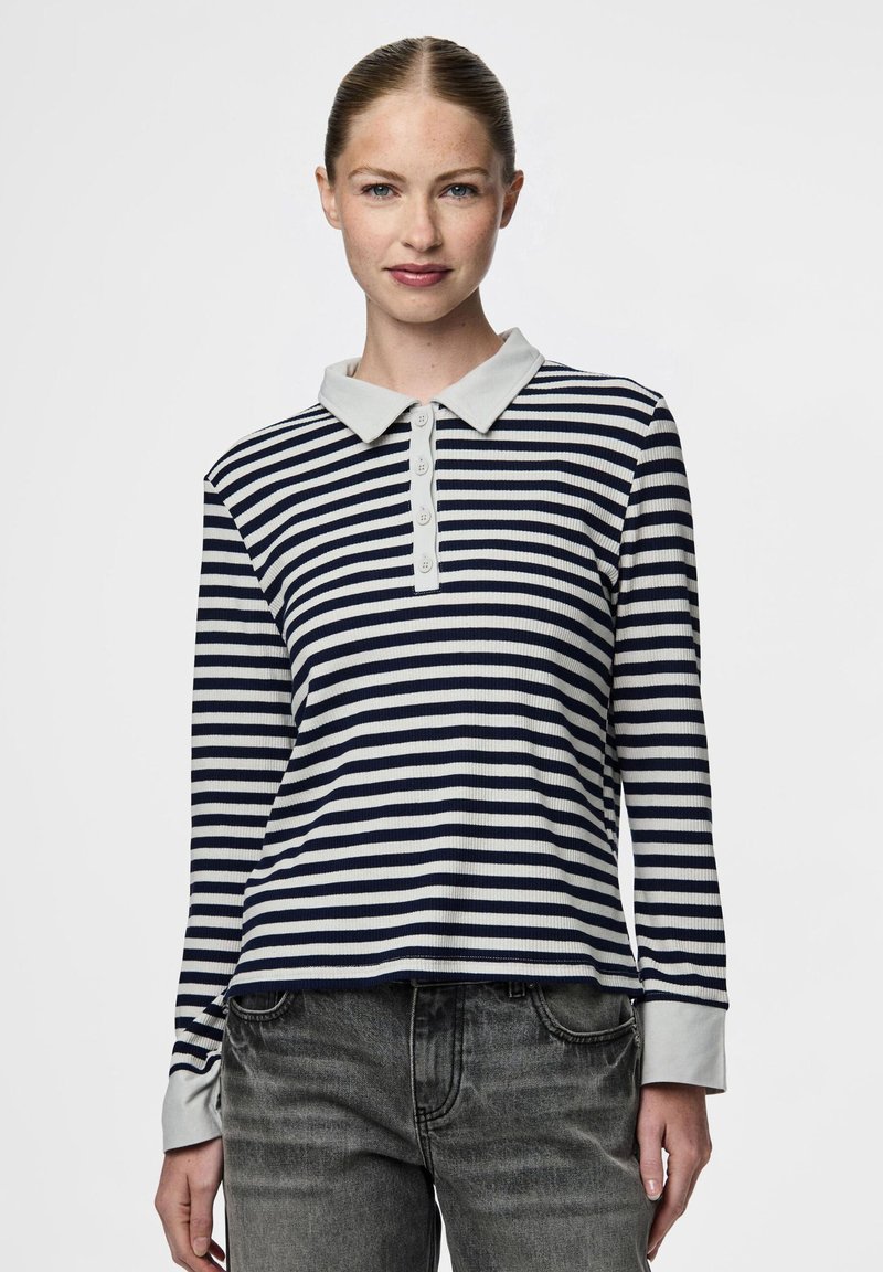 Ilgų rankovių polo marškiniai, kuriuose yra tamsiai mėlynos ir baltos horizontalios juostelės, šviesiai pilkas apykaklė ir penkių mygtukų apykaklė. Minkšta, tekstūruota medžiaga.