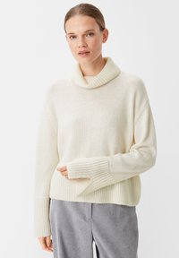 Beige gestrickter Pullover mit einem Rollkragen, weiten Ärmeln und gerippte Bündchen. Weiche Textur mit einer lockeren Passform, kombiniert mit grau gestreiften Hosen.