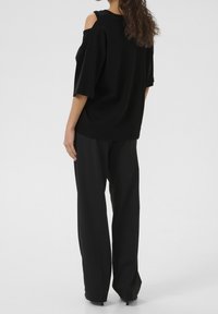Sort oversized t-shirt med skulderskæringer, korte ærmer og løs pasform, parret med sorte vide bukser. Glat stoftekstur.
