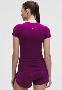 Lühikeste varrukatega, keha lähedal istuv lilla sportlik topp, millel on tekstuuriga kangas ja seljal väike logo, koos vastavate lühikeste pükstega.