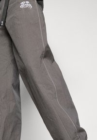 Gray waterproof fabric garment with white stitching and subtle branding. Features an adjustable fit with a relaxed silhouette.