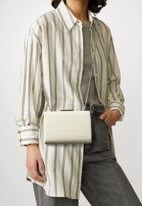 Valkoinen tekonahkainen läppälaukku, jossa on krokotiilinanomainen pinta, suorakulmainen muoto ja ketjuhihna, joka on käytössä raidallisen paidan kanssa.