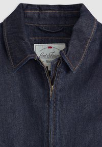Veste en denim bleu foncé, avec une fermeture à glissière sur le devant, un col pointu et des coutures orange contrastantes. Étiquette Levi's visible à l'intérieur de l'encolure.