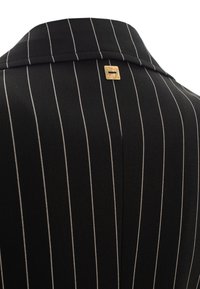 Blazer nero a righe con colletto strutturato, dotato di un'etichetta con logo dorato vicino al colletto, realizzato in un tessuto liscio.
