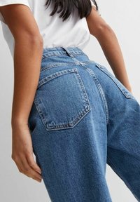 Högmidjade, blå denimjeans med avslappnad passform. Har två bakfickor och synliga sömdetaljer. Tyg av bomull med en något texturerad yta.