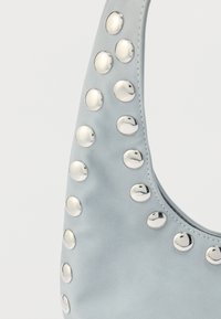 Sac en cuir bleu clair avec des clous métalliques ronds sur le côté, une texture lisse et une forme courbée. Bretelle réglable incluse.