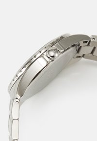 Montre en acier inoxydable avec une finition métallique lisse, boîtier rond, lunette texturée et couronne marquée. Présente un design de bracelet à maillons.
