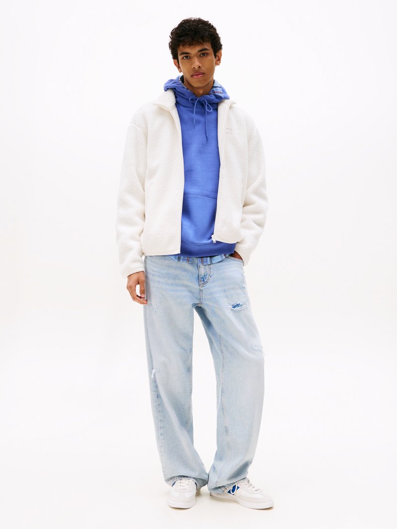 Witte fleecejas over een blauwe hoodie, lichtblauwe distressed jeans en witte sneakers met blauwe accenten. Casual outfit met zachte texturen.