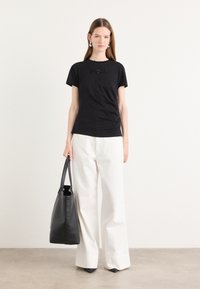 T-shirt nera a maniche corte con decorazioni testurizzate sul petto, abbinata a pantaloni bianchi a gamba larga e una borsa a tracolla in pelle nera.