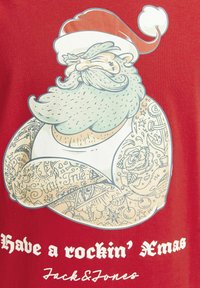 Rød t-shirt med et grafik af en tatoveret julemand med hvidt skæg og juleskæg. Teksten lyder "Have a rockin' Xmas" i fed hvid skrift.