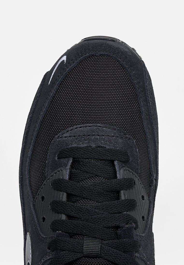 Baskets Nike noires avec textures en mesh et suède, lacets noirs et logo Nike blanc en forme de virgule près de la zone des orteils, vues de dessus.