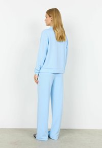 Conjunto de ropa cómoda color azul claro que incluye una camiseta de manga larga y pantalones de pierna ancha. Tejido suave con textura lisa y corte relajado.