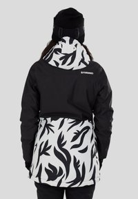 Zwart-wit gestreepte skijas met een bladdesign op de onderste helft en een effen zwarte bovenkant, met een capuchon die over het hoofd kan worden getrokken.