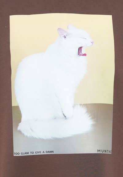 Brązowa koszulka z białym kotem ziewającym na żółtym tle. Poniżej znajduje się tekst "ZA BARDZO GLAM, ŻEBY SIĘ PRZEJMOWAĆ", a także nazwa marki "MUNTHE."