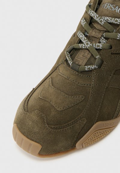 Olive roheline seemisnahast toss, mis on tekstureeritud disainiga, sisaldab toonitud õmblusi, mustrilisi paelu ja kummist tallaga, millel on geomeetrilised aktsendid.