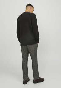 Maglione nero con texture, orlo a coste, abbinato a pantaloni grigi a scacchi. Modello posizionato con le mani in tasca, visto di spalle.