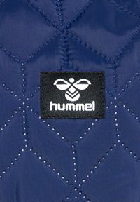 Marine geweven stof met een geometrisch gestikt patroon, met een zwart label dat een wit logo toont en de tekst "hummel."