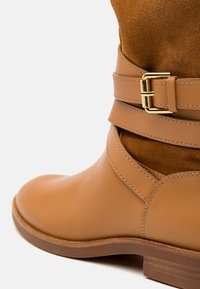 Bottine marron clair en cuir avec tige en daim, design à double bride avec boucle dorée, bout arrondi lisse et semelle texturée.