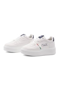 Valkoiset alusta-tennarit, joissa on sileä nahkasynteeri, tummansiniset yksityiskohdat kantapäässä ja huomaamattomat ilmanvaihtoreijät. Koristeena punaiset ja vihreät raidat.