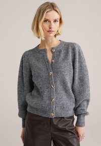 Grå stickad kofta med rund halsringning, ribbad struktur och sex knappar i guldfärg framtill. Puffärmar och åtsittande muddar.