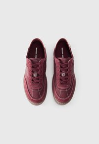 Burgundy sneakers with a smooth texture, featuring a tonal design, contrasting white stitching, and a brown rubber sole.