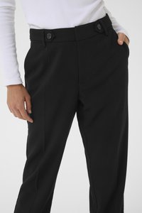 Black tailored pants feature a smooth texture, angled front pockets, and button closures with hexagonal accents. Fit shown is slim.