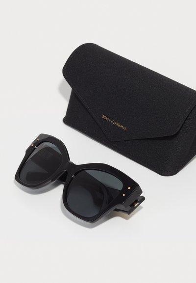 Ochelari de soare negri, supradimensionați, cu lentile închise la culoare și accente aurii. Însoțiți de un toc din material textil negru, cu închidere magnetică și detalii cu logo.