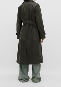 Ciemnozielony, długi trencz z paskiem w talii, dużym kołnierzem i zapinanymi mankietami. Noszony na szerokich, luźnych jasnoniebieskich dżinsach.