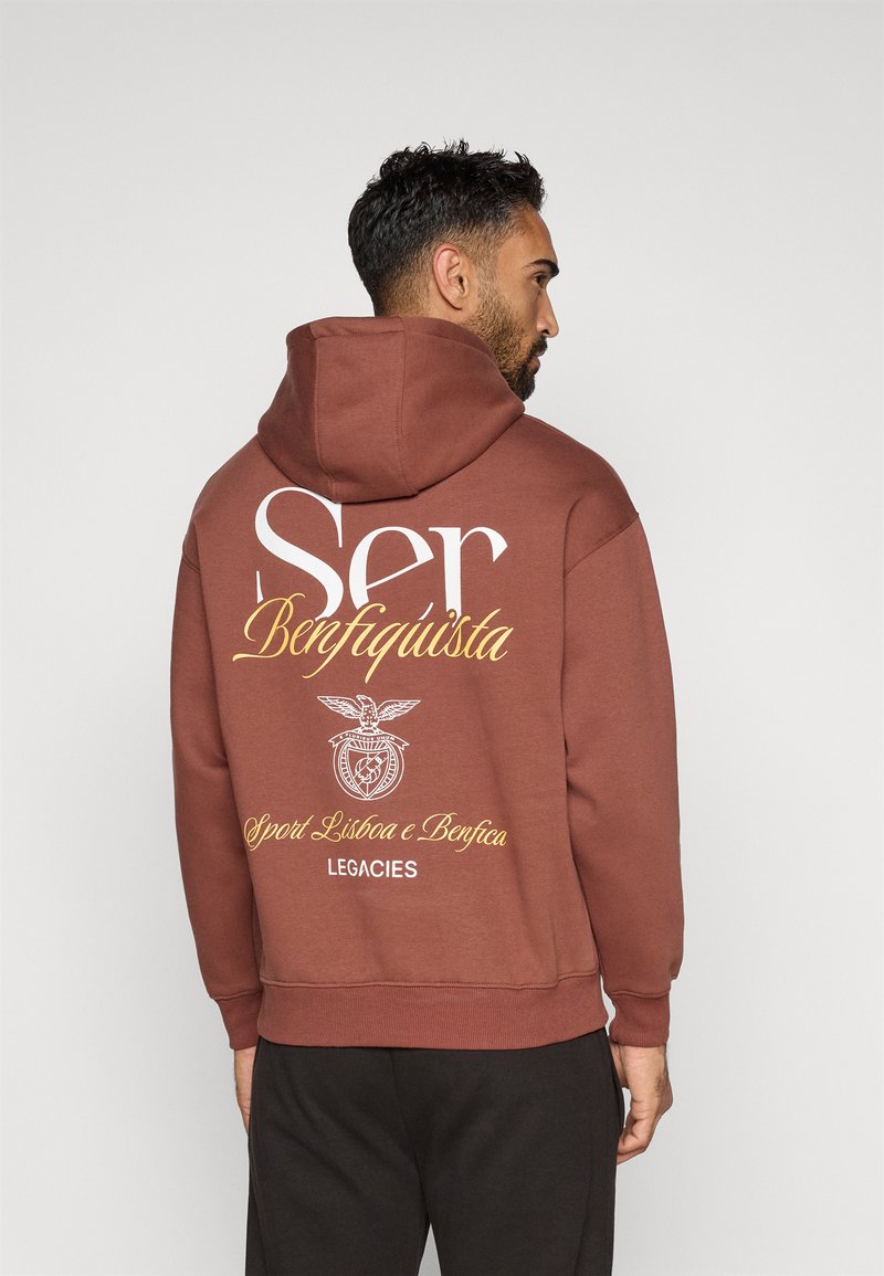 Brązowa bluza z kapturem z dużą białą i żółtą grafiką na plecach, z tekstem i emblematem. Miękki materiał, luźny krój i kaptur ze sznurkiem.