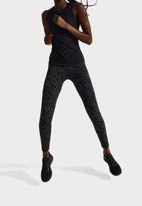 Černý sportovní top spárovaný s těsnými černými legínami s kontrastním grafickým vzorem, doplněný černými teniskami.