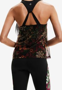 Mustaton ilmanhihaisen toppi, jossa on solmuelementti takana, päälle puettu läpikuultavasta kukkakuosisesta materiaalista vihreän, punaisen ja beigen sävyissä.