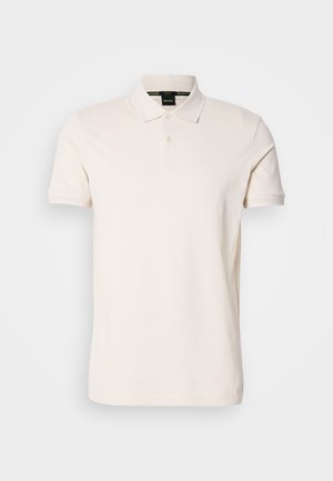 Camisa polo na cor creme, feita de tecido suave, com um colarinho clássico, dois botões e um discreto detalhe do logotipo no peito.