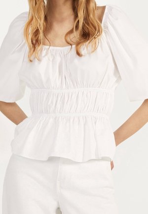Witte peplumtop van lichtgewicht stof met een vierkante halslijn, pofmouwen en een gesmockte taille. Soepele textuur en een ontspannen pasvorm.