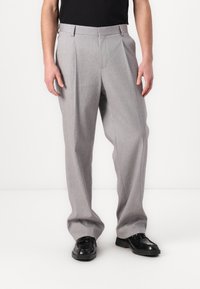 Graue, maßgeschneiderte Hose mit strukturierter Oberfläche, mit Falten, geraden Beinen und hohem Bund, kombiniert mit schwarzen Lederschuhen.